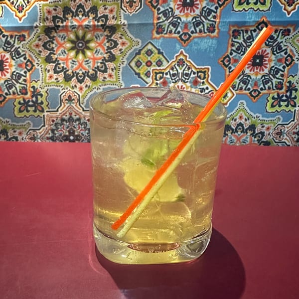 A refreshing El Nopal cocktail with lime and ice, served with an orange straw.