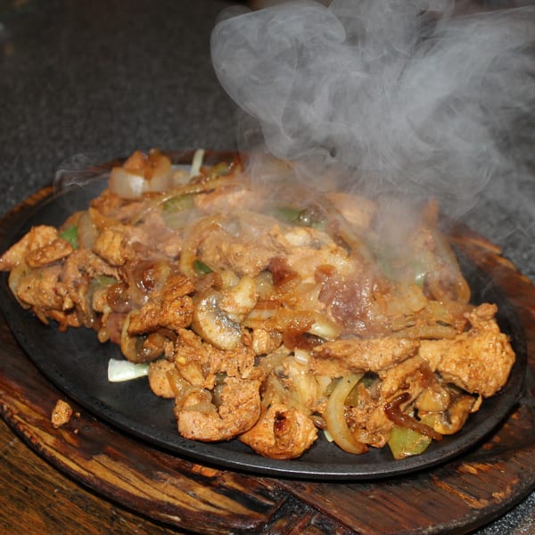 Sizzling chicken fajitas with onions, mushrooms, and bell peppers on a hot skillet at El Nopal.