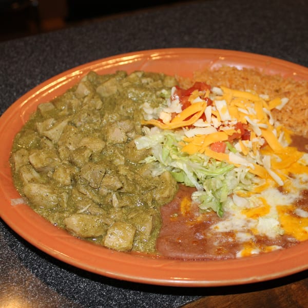 El Nopal's green chile chicken, refried beans with cheese, rice, and salad on an orange plate.