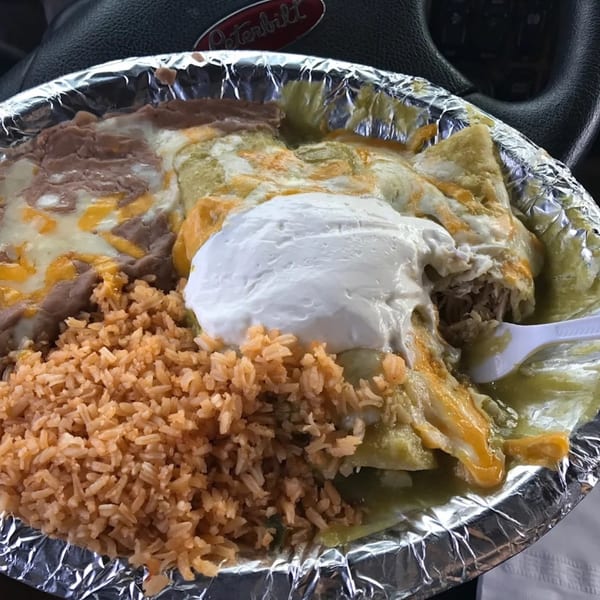 El Nopal's chicken enchiladas with green sauce, rice, refried beans, and sour cream in a foil container.