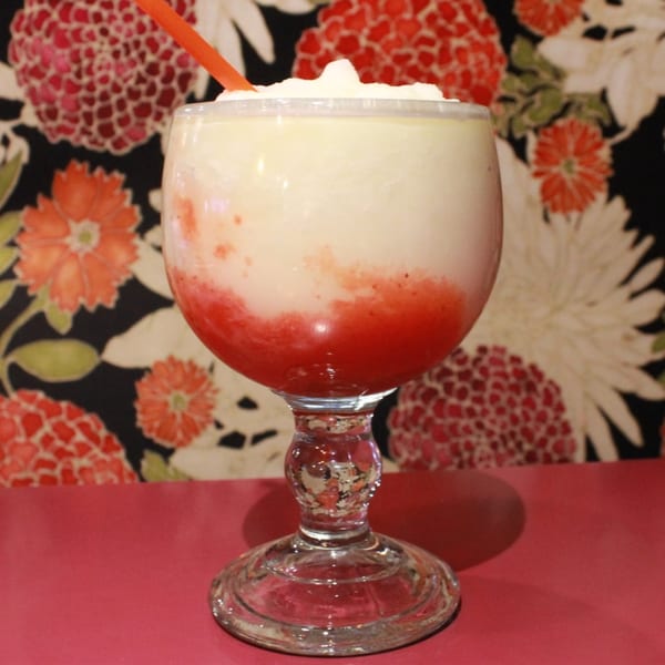 Strawberry and lime margarita in a goblet with a red straw, against a floral background.