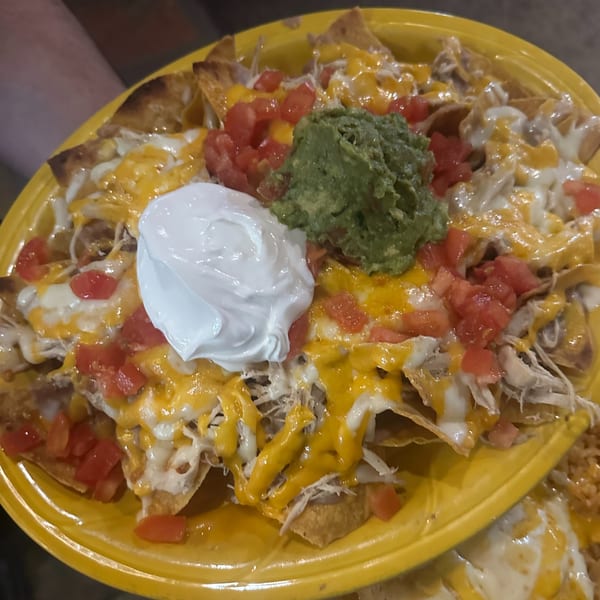A vibrant yellow plate piled high with chicken nachos, topped with guacamole, sour cream, and diced tomatoes.