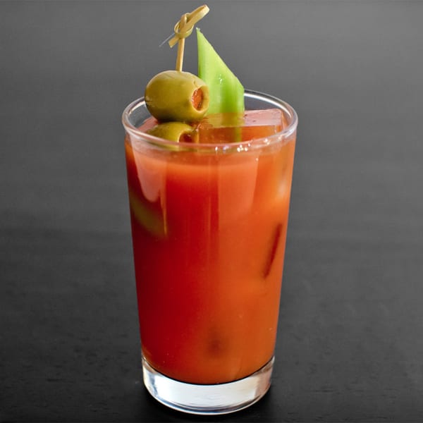 A vibrant red Bloody Mary cocktail in a glass, garnished with green olives and a celery stalk.