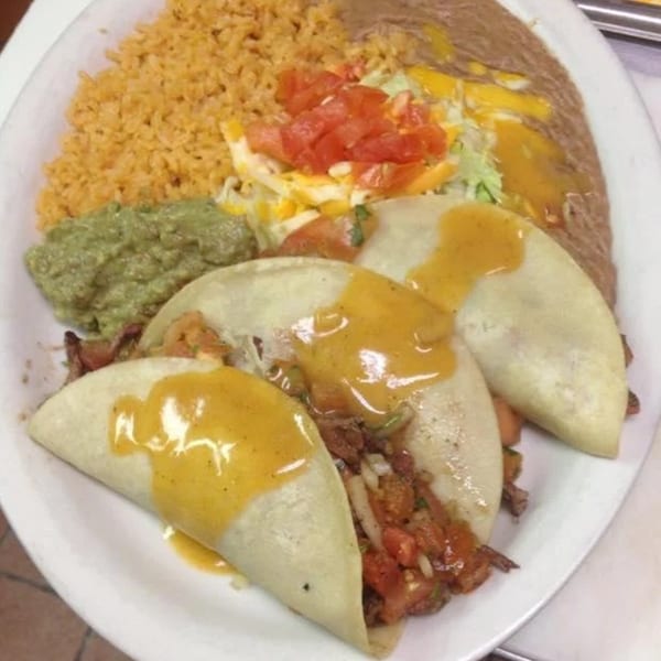Three tacos with cheese sauce, rice, refried beans, guacamole, and a side salad.